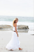 A blonde woman by the sea wearing a white summer dress
