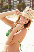 A young brunette woman on a beach wearing a green bikini with a summer hat