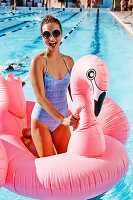 A young blonde woman wearing a blue bathing suit keeling on an inflatable swan