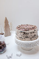 A chocolate cake on a cake stand on a table decorated for Christmas