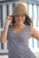 A young brunette woman on a beach wearing a blue-and-white striped top and a summer hat