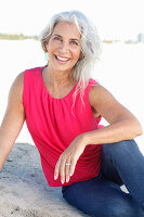 A mature woman with white hair on a beach wearing a pink top and blue jeans