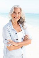 A mature woman with white hair on a beach wearing a striped blouse and a top