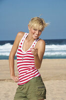 A blonde woman with short hair by the sea wearing shorts and a red-and-white striped top