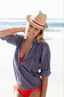 Blonde Frau mit Hut in rotem Bikini und blauer Bluse am Strand