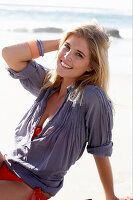 A blonde woman on a beach wearing a red bikini and a blue blouse