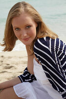 A young woman on a beach wearing a white summer dress and a striped cardigan