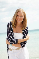 A young woman on a beach wearing a white summer dress and a striped cardigan