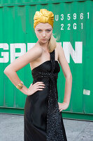 A young blonde woman wearing a black evening dress and a golden headscarf