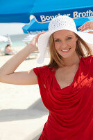 A blonde woman on a beach wearing a red top and a white hat