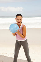 Junge brünette Frau in sportlicher Kleidung mit Ball am Meer