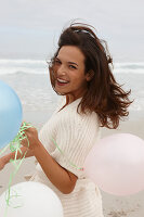 A brunette woman wearing a short-sleeved cardigan and holding balloons