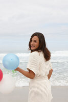 A brunette woman wearing a short-sleeved cardigan and holding a balloon