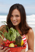 Junge brünette Frau mit Gemüseschale im Bikinoberteil am Strand