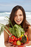 A young brunette woman on a beach holding a bowl of vegetables
