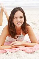 Brünette Frau in weißem Sommerkleid auf rosa Tuch liegend am Meer