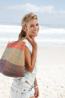 A blonde woman on the beach wearing a light t-shirt and denim shorts holding a wicker bag
