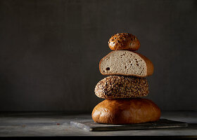 Drei Brote und ein Brötchen, gestapelt vor dunklem Hintergrund