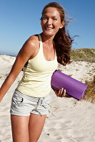 A brunette woman on a beach with a mat wearing a light top and shorts