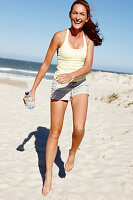 Brünette Frau mit Wasseflasche in hellem Top und Shorts am Strand