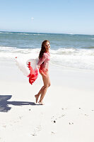 Brünette Frau mit Strandtuch in rosa Bluse und Bikini am Meer