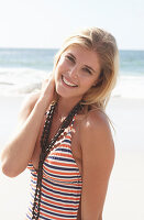 A young blonde woman on a beach wearing a striped swimsuit