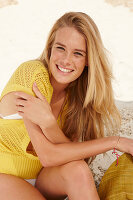 A blonde woman on a beach wearing a yellow knitted top