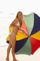 Blonde Frau mit Sonnenschirm in weißem Bikini am Strand