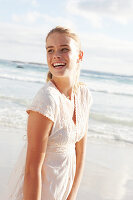 A blonde woman by the sea wearing a white embroidered dress