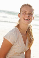 A blonde woman by the sea wearing a white embroidered dress