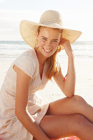 Blonde Frau mit Hut in weißem Kleid am Meer