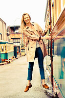 A young blonde woman wearing a trench coat holding onto a tram door