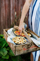 A woman carrying a wooden crate with tarts for a picnic