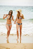 Two women wearing bikinis and summer hat on the beach