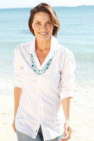 A brunette woman on a beach wearing a white shirt