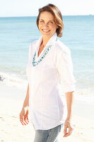 A brunette woman on a beach wearing a white shirt