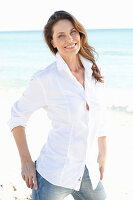 A brunette woman on a beach wearing a white shirt