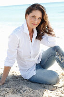 Brünette Frau in weißem Hemd und Jeans am Strand