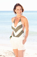 Brünette Frau in gestreiftem Badeanzug und weißen Shorts am Strand