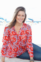 A blonde woman on a beach wearing a tunic with a floral pattern and jeans