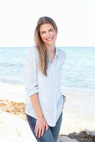 A young woman by the sea wearing a light blue shirt and jeans
