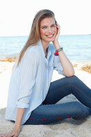 A young woman by the sea wearing a light blue shirt and jeans