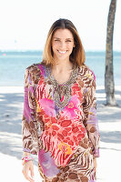 A brunette woman by the sea wearing a colourful beach dress