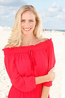 A blonde woman on a beach wearing a red dress
