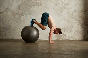 A young man doing a handstand with his feet on a physio ball