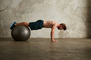 A young man doing push-ups with his knees on a physio ball