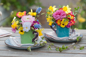 Kleine Frühlings-Tischdekoration mit bunten Sträußchen in Tassen