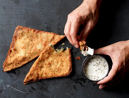 Hands dipping Bolani in yogurt sauce