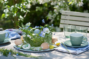 Easter table decorations on the terrace with horned violets, grasses, Easter eggs and a candle