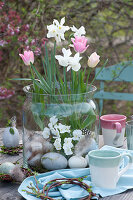 Daffodils 'Toto', tulips and horned violets without soil in the glass, Easter eggs and willow wreaths as decorations